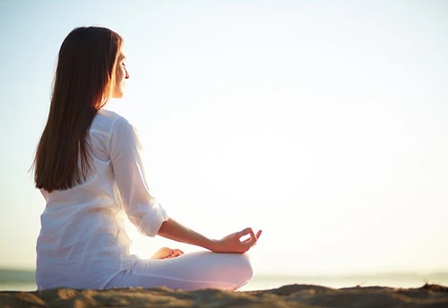 A woman meditating quietly on a beach in soft morning light